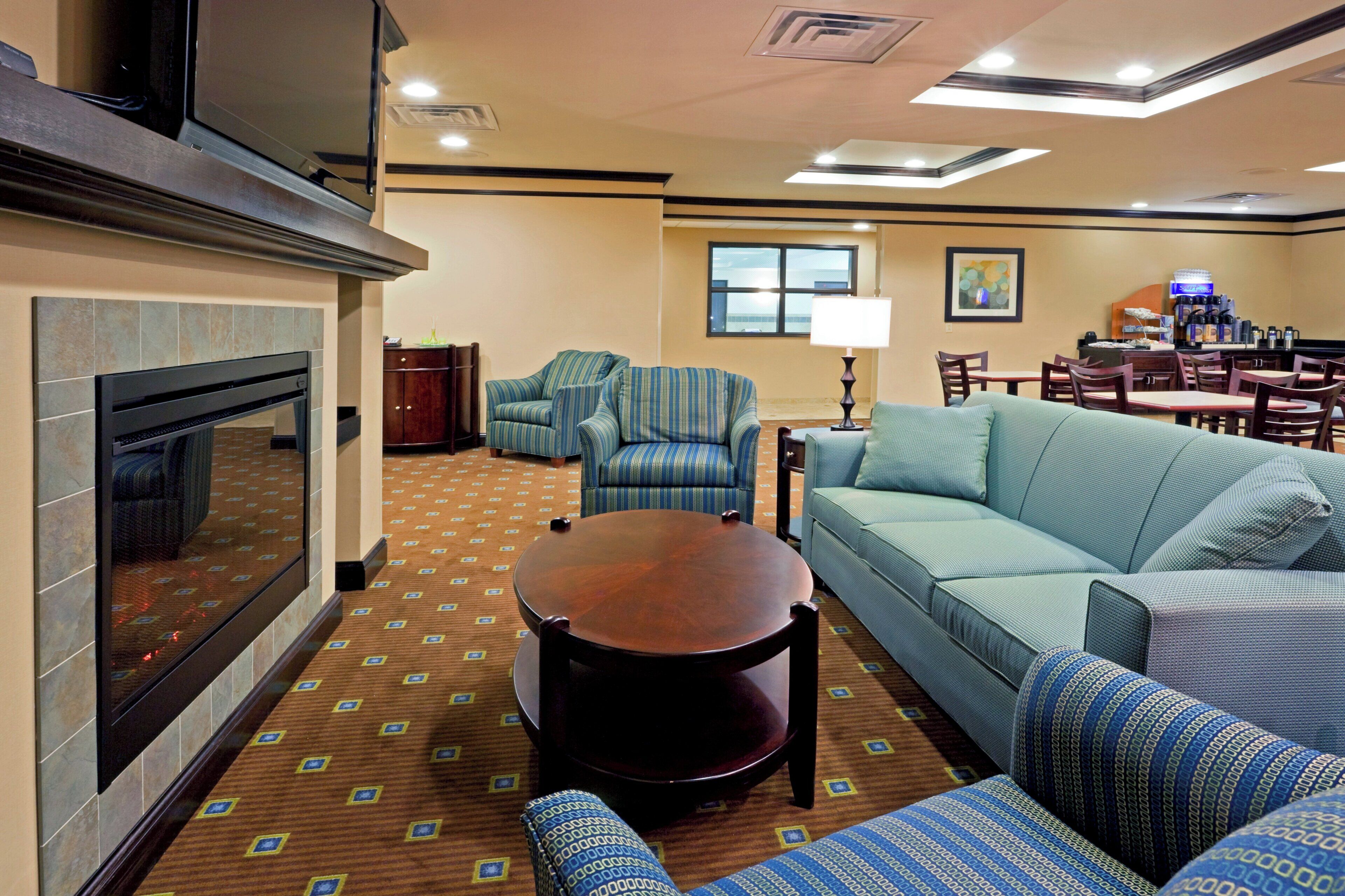 A hotel lounge with a fireplace, sofas, armchairs, a dining area, and a coffee station.