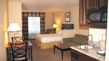 A hotel room with a bed, a sofa, a desk, a chair, a microwave, a sink, and a window with curtains.