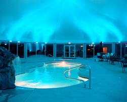 Piscina interior com barreira de vidro, rodeada por uma área coberta com assentos e vista para o exterior.