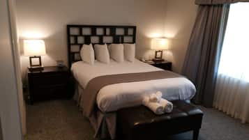 Une chambre d’hôtel avec un grand lit, deux tables de chevet avec des lampes, un banc avec des serviettes et une fenêtre avec des rideaux.
