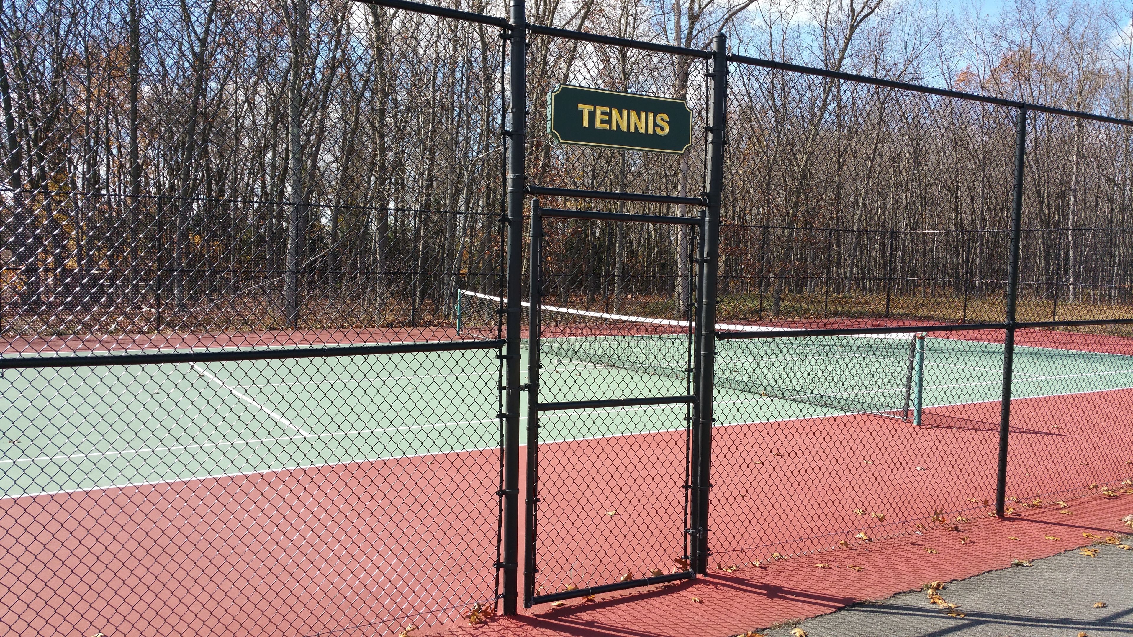 Een tennisbaan met een bord waarop 'TENNIS' staat en een hek van gaas.