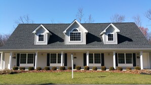 A two-story house with a gabled roof, dormer windows, and a covered front porch with columns. - The Village At Pocono (Blakeslee)