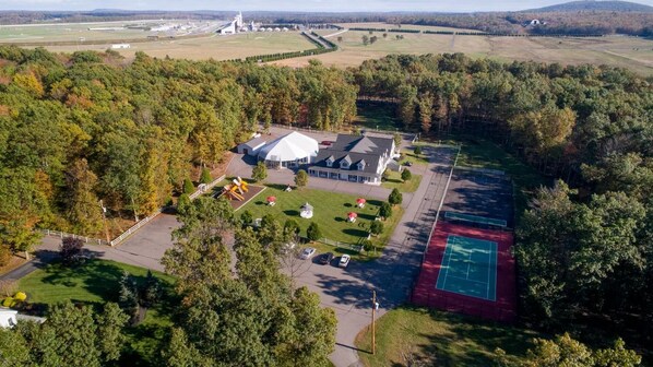 An aerial view of a property with a large house, tennis court, and surrounding wooded area.