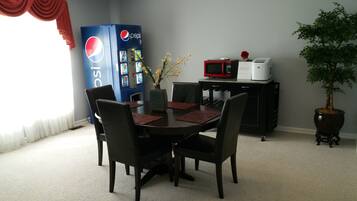Een eethoek met een tafel voor vier personen, een Pepsi-koelkast, een magnetron en een potplant.