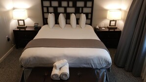 A hotel room with a large bed, two bedside tables, a headboard with a grid pattern, and two lamps. - The Village At Pocono (Blakeslee)
