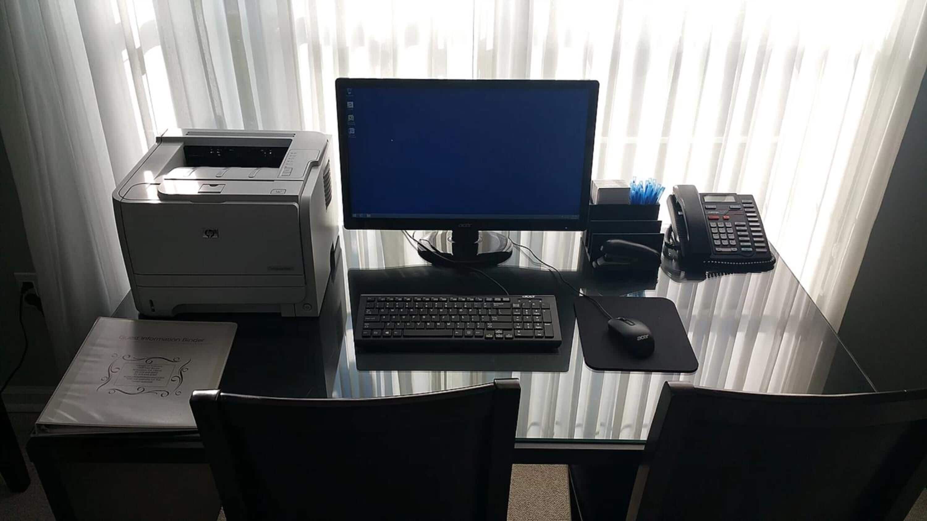 Ein Computertisch mit einem Desktop-Computer, Tastatur, Maus und Drucker.