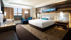 Een hotelkamer met een groot bed, een bureau met stoel, een televisie en een raam met gordijnen.
