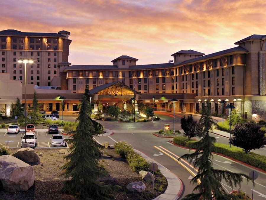 A large hotel with a central entrance, multiple floors, and a parking lot with several cars.