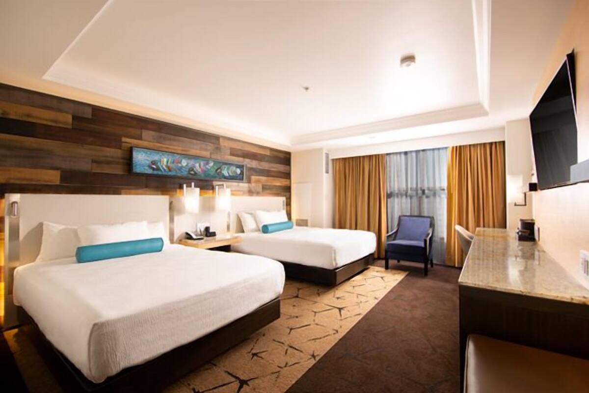 A hotel room with two beds, a desk, a chair, and a television.