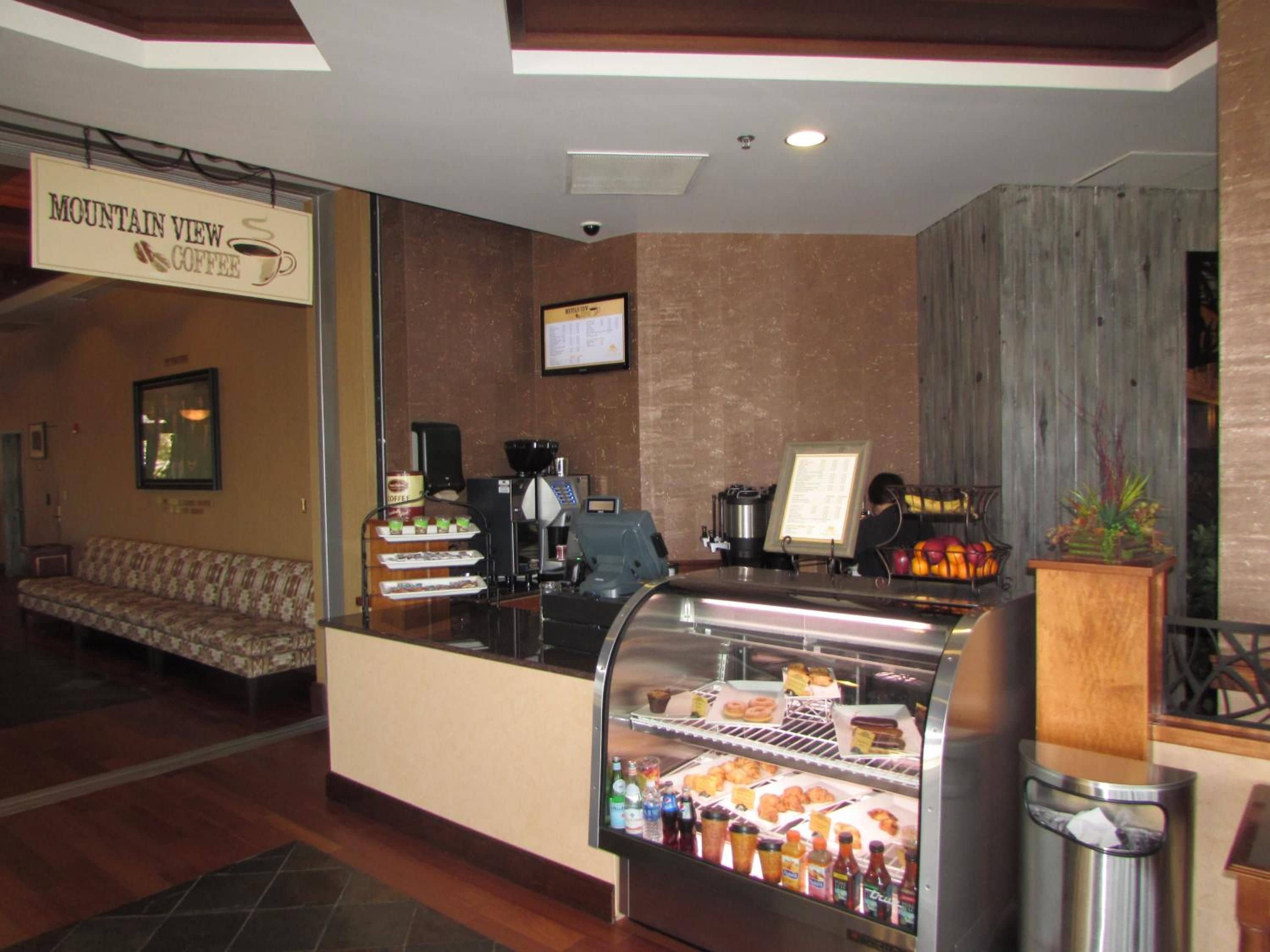 Café com balcão, máquina de café e vitrine com doces e bebidas.