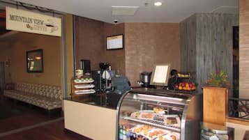 Café com balcão, máquina de café e vitrine com doces e bebidas.