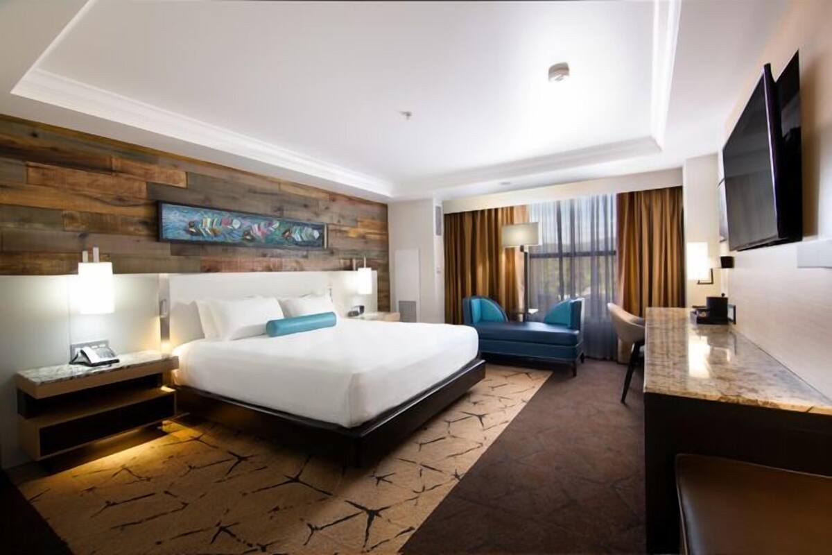 A modern hotel room with a large bed, a desk, a flat-screen TV, and a wooden accent wall.