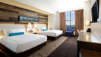 A hotel room with two beds, a desk, a TV, and a large window with a view.