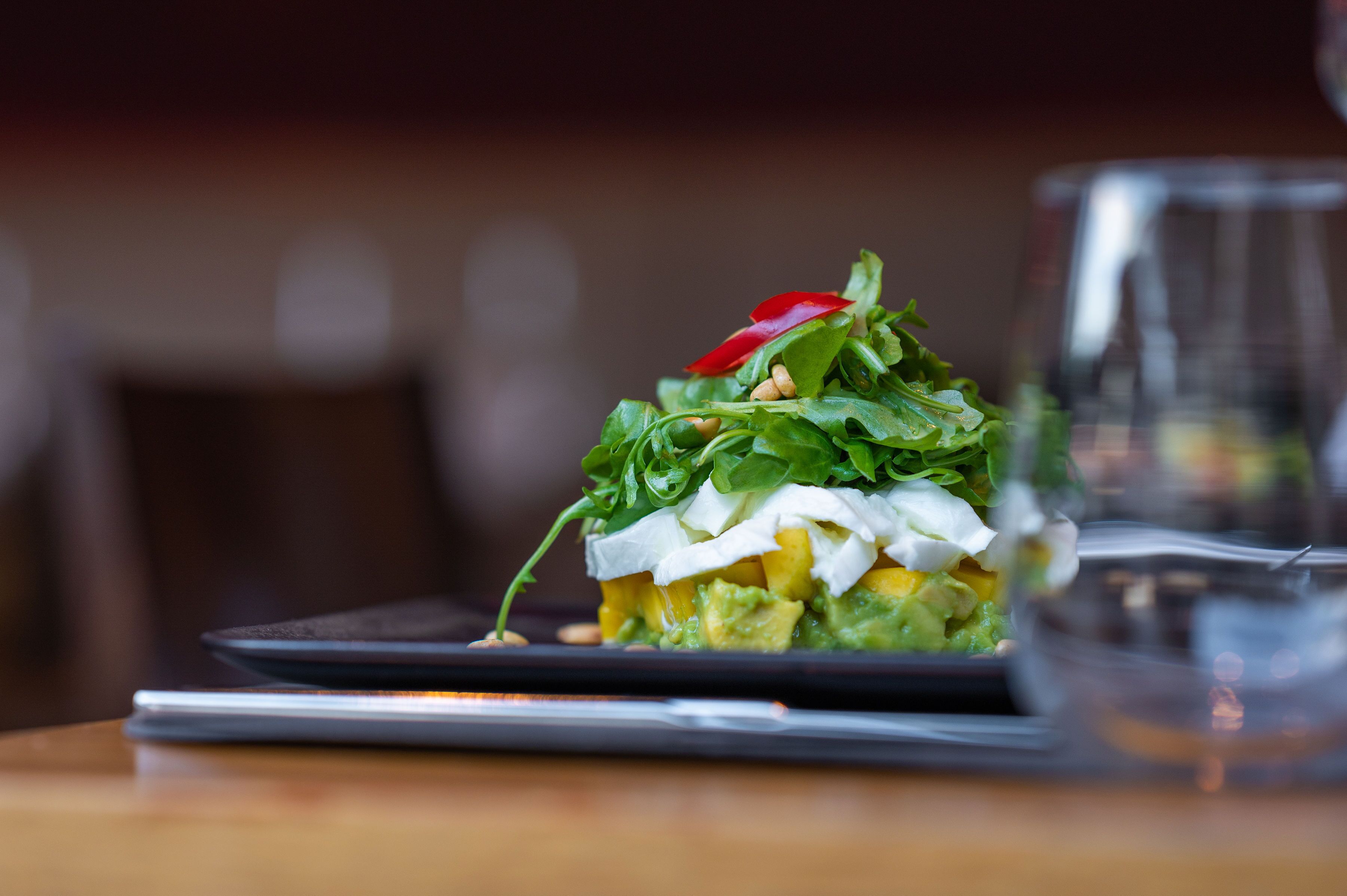 Une salade joliment présentée dans une assiette noire, accompagnée d’un verre d’eau.
