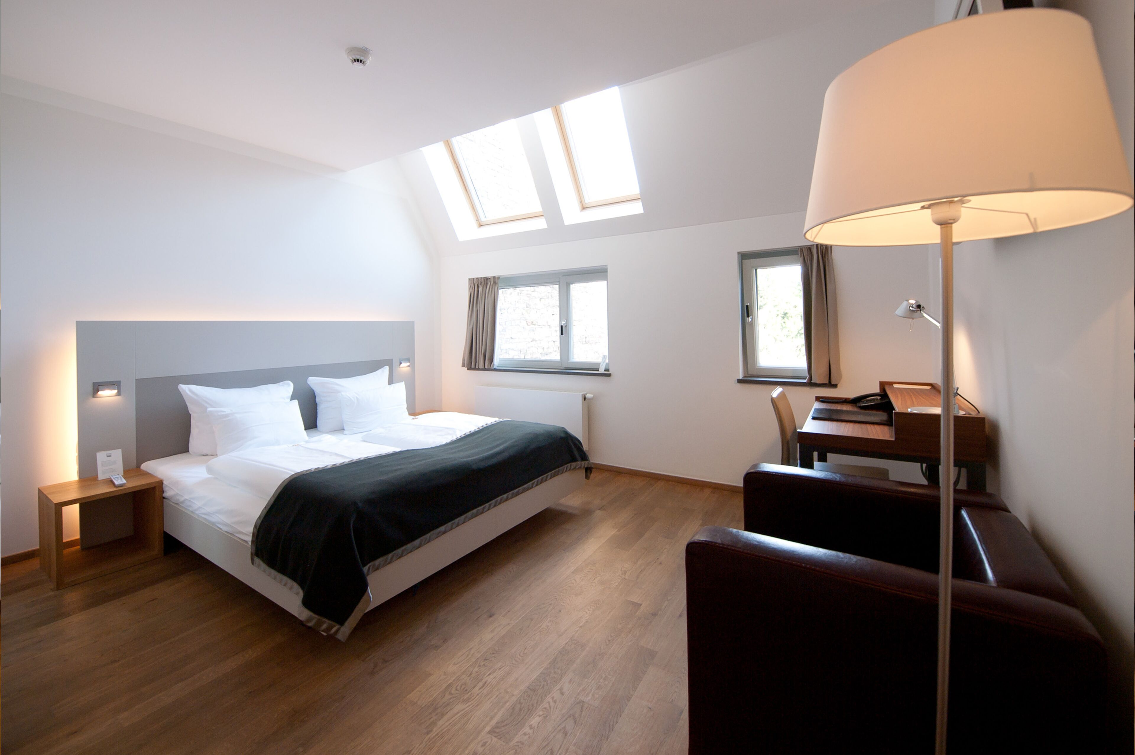 Una habitación de hotel moderna con cama, mesitas de noche, escritorio, silla y tragaluces.
