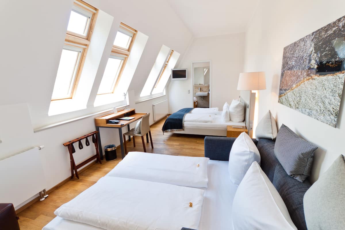 Habitación de hotel con dos camas, un escritorio, una silla, un televisor, una lámpara y un cuadro.