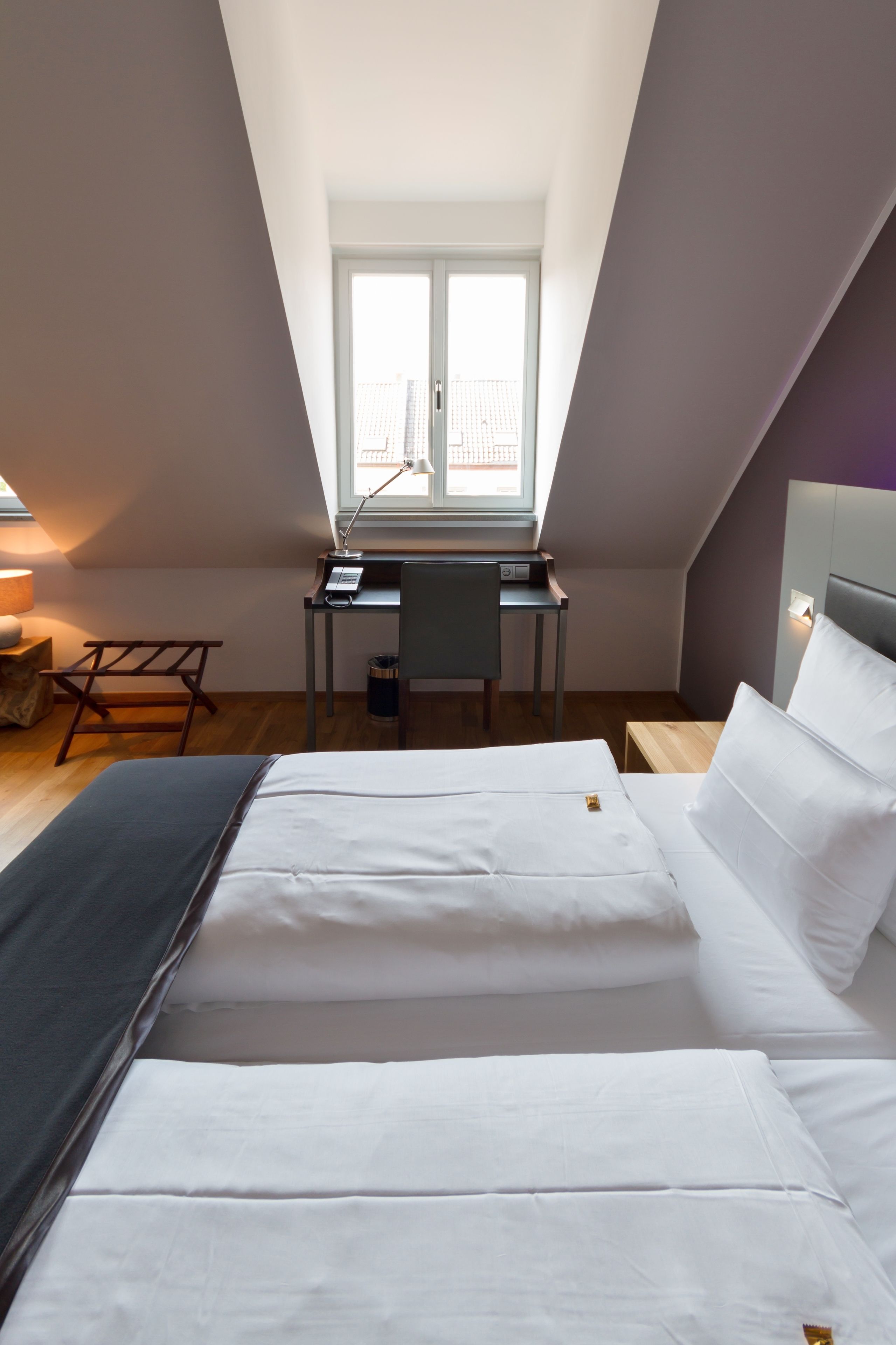 Une chambre avec un lit, un bureau et une chaise. Il y a une fenêtre au-dessus du bureau.