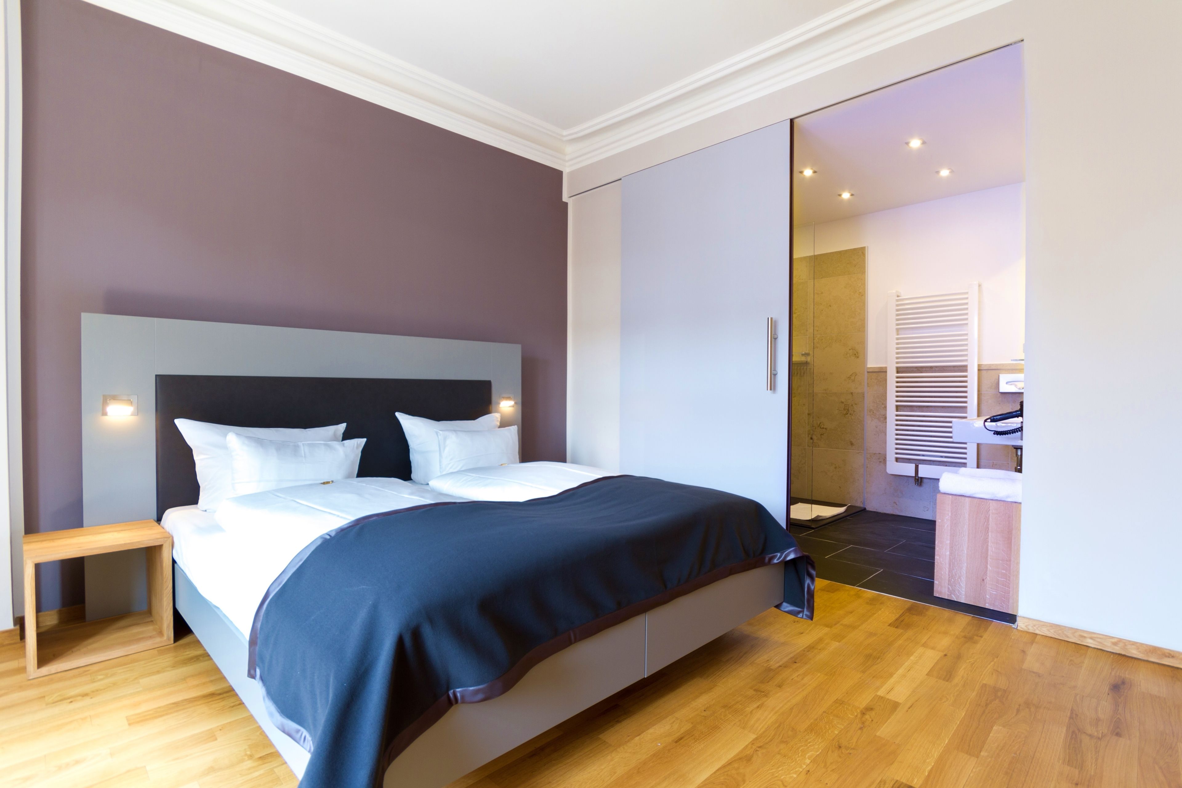 Ein modernes Schlafzimmer mit einem großen Bett, Holzboden und einer Schiebetür zu einem Badezimmer.