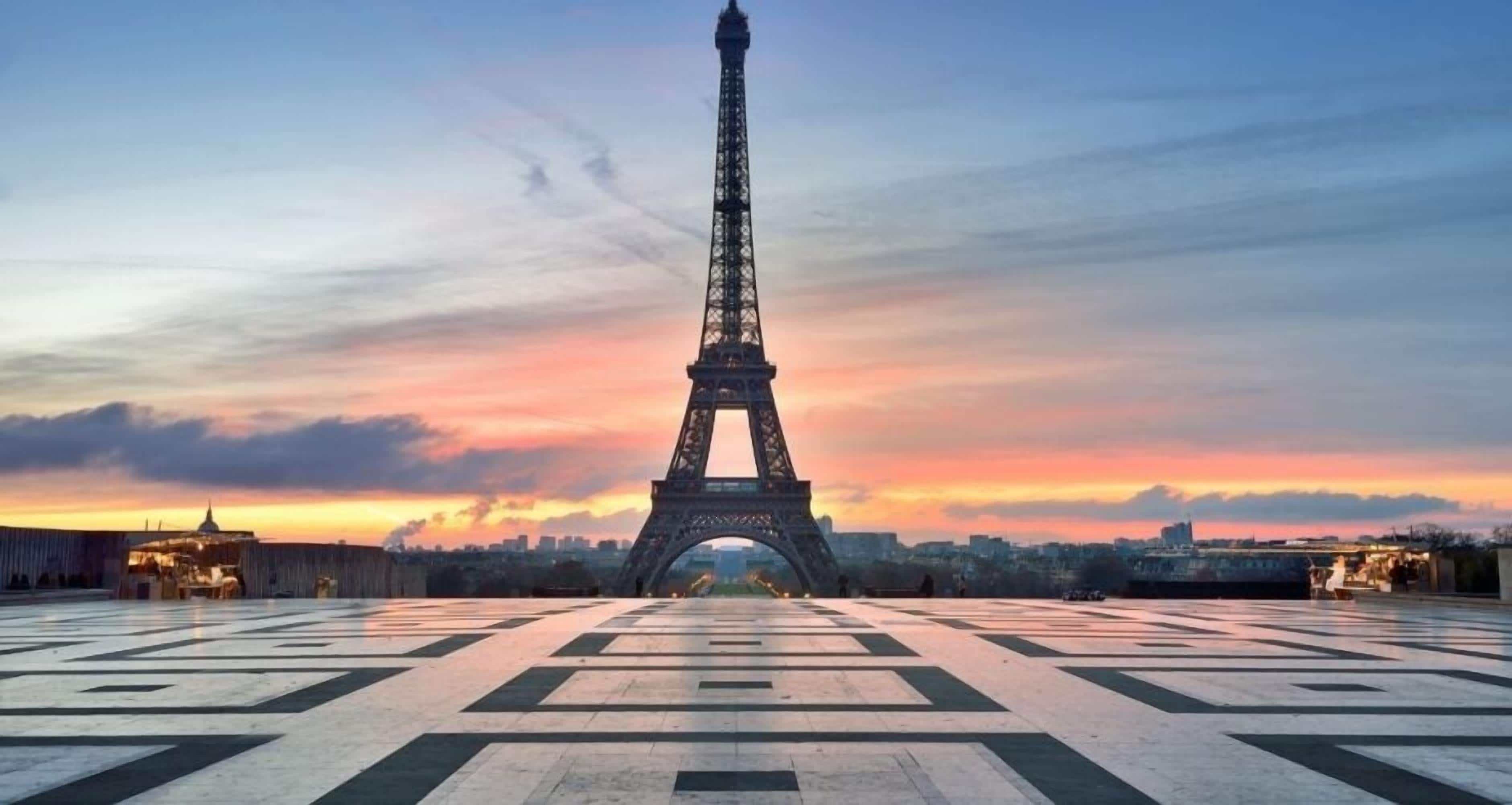 The Eiffel Tower at sunset with a tiled plaza in the foreground.