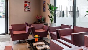 Eine Lobby mit roter Sitzgelegenheiten, einem Couchtisch mit Zeitschriften, einer Zimmerpflanze und einem großen Fenster.