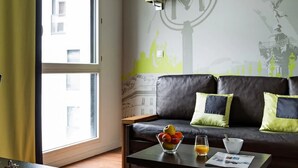 Ein modernes Wohnzimmer mit einer Couch, einem Couchtisch mit einer Obstschale und einem Glas Orangensaft, sowie einer Wand mit einem Stadtbild-Wandgemälde.