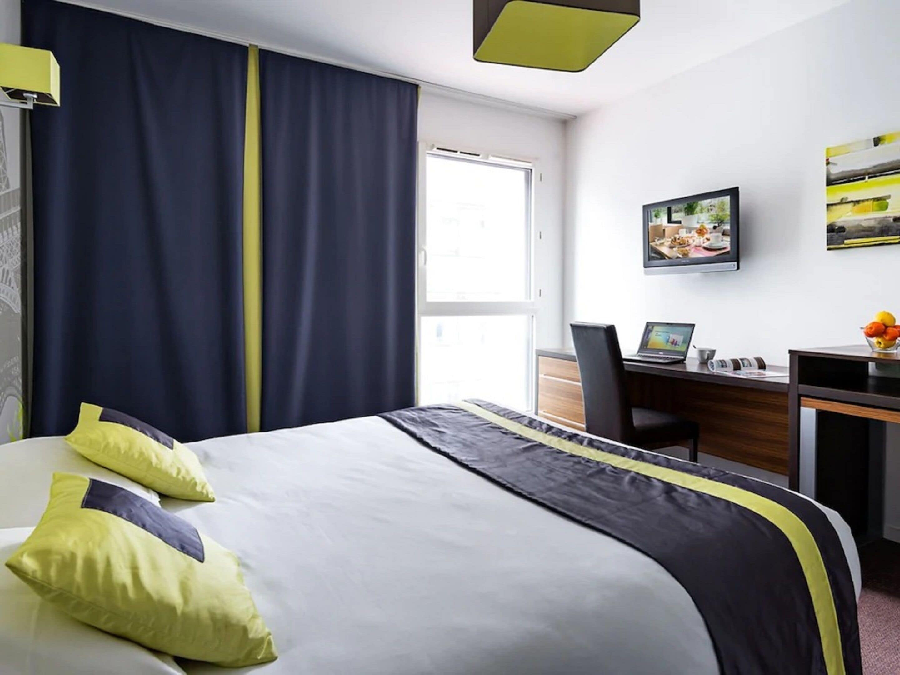 Una habitación de hotel con una cama, un escritorio, una silla, una computadora portátil y un cuadro en la pared.