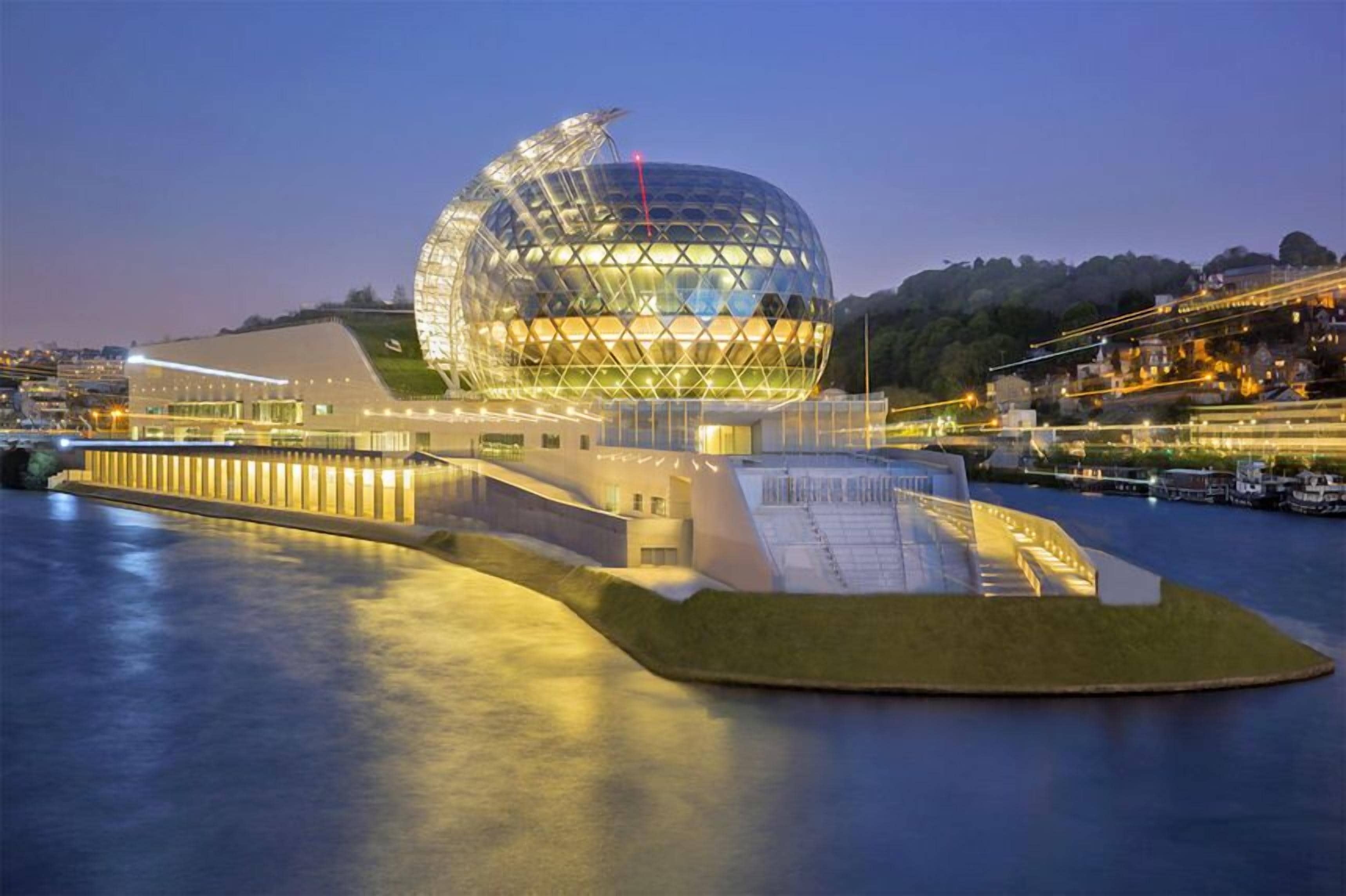 A modern architectural structure with a large dome and a waterfront setting.