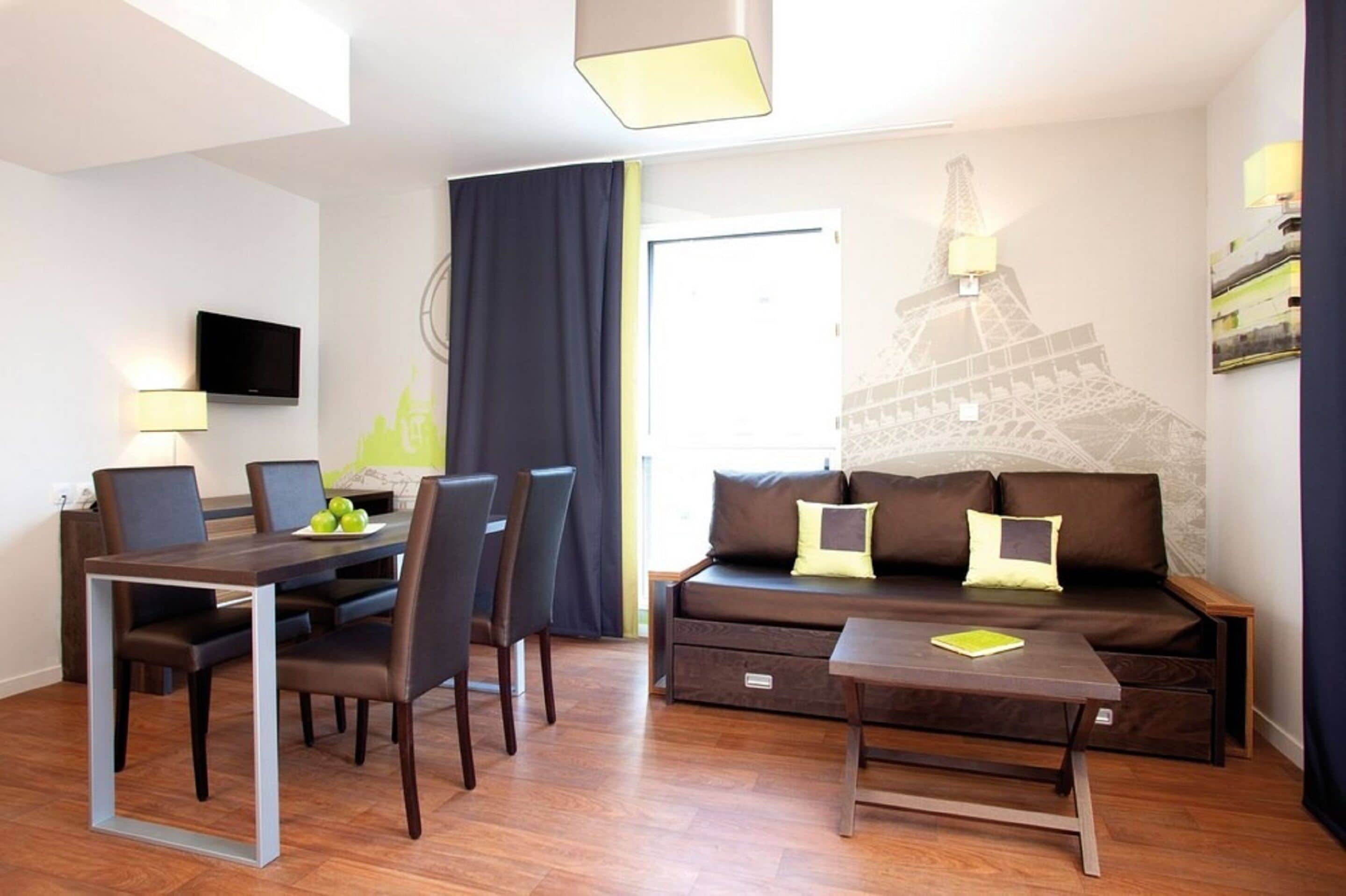 A modern hotel room with a dining area, a sofa, and a wall mural of the Eiffel Tower.
