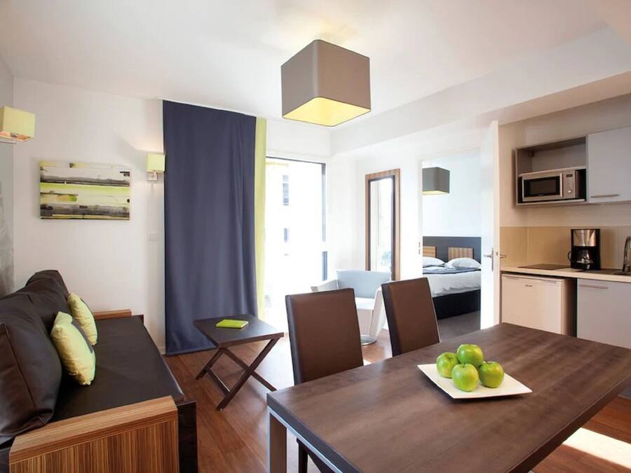 Quarto de hotel moderno com uma mesa de jantar de madeira, um sofá e uma área de cozinha.