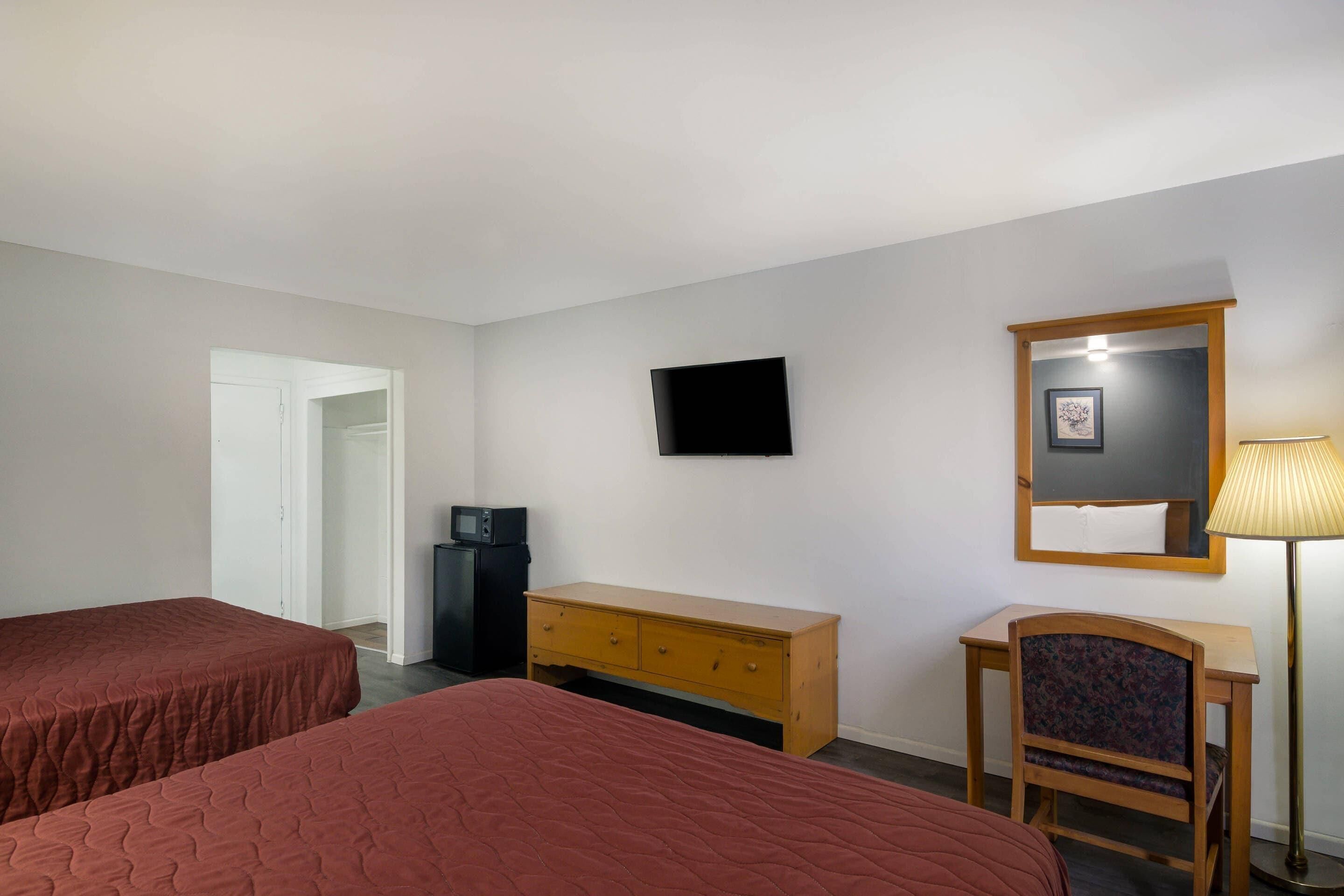 A hotel room with two beds, a TV, a desk, a chair, a lamp, and a wardrobe.