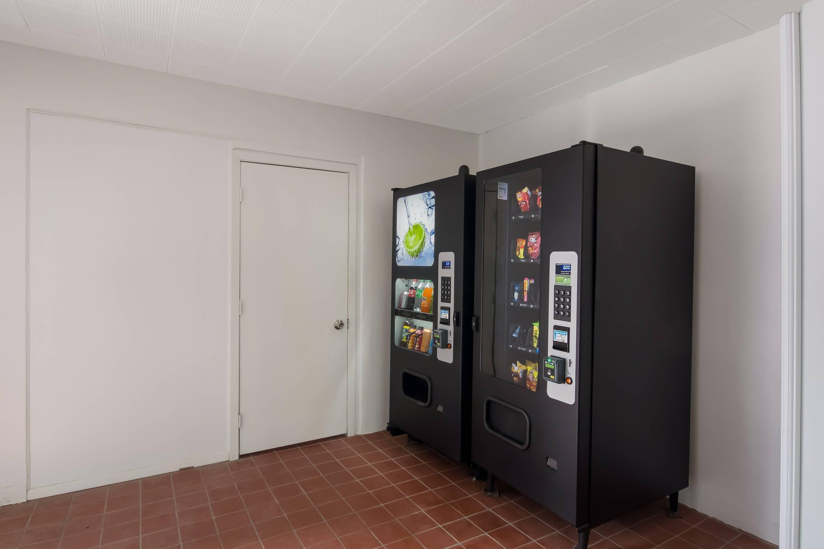 Una habitación con dos máquinas expendedoras, una puerta blanca y suelo de baldosas.