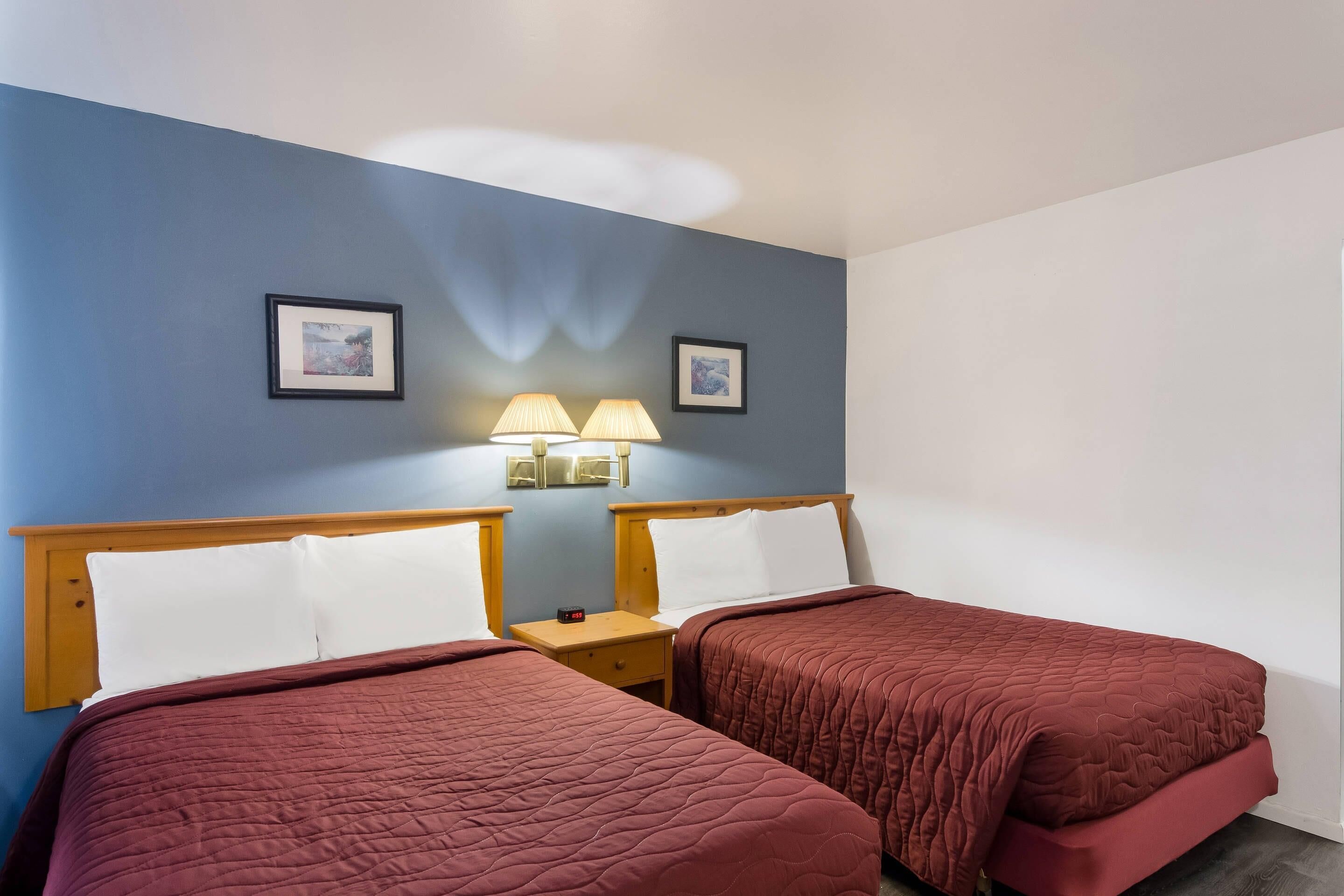 Ein Hotelzimmer mit zwei Betten, einem Nachttisch mit Lampe und zwei gerahmten Bildern an der Wand.