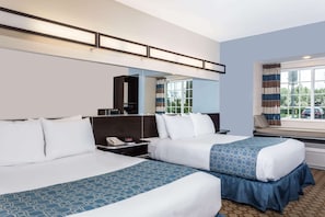 A hotel room with two beds, a large window with curtains, a desk with a telephone, and a mirror above the bed.