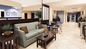 A hotel lobby with a reception desk, seating area with a sofa and chairs, and a kitchenette in the background. - Microtel Inn & Suites by Wyndham Spring Hill/Weeki Wachee (Spring Hill)