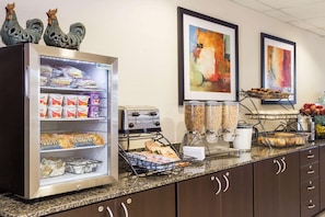 A self-service breakfast station with a refrigerated display, coffee machine, and various food items.