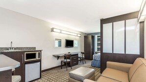 A compact hotel room with a kitchenette, a small dining table, a sofa, and a TV. - Microtel Inn & Suites by Wyndham Spring Hill/Weeki Wachee (Spring Hill)