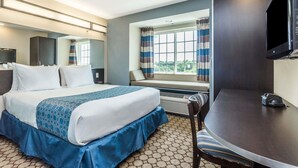 A hotel room with a bed, a desk, a chair, a TV, and a window with curtains. - Microtel Inn & Suites by Wyndham Spring Hill/Weeki Wachee (Spring Hill)