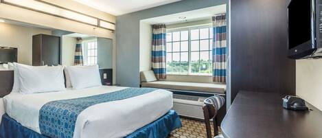 A hotel room with a bed, a desk, a chair, a TV, and a window with curtains.