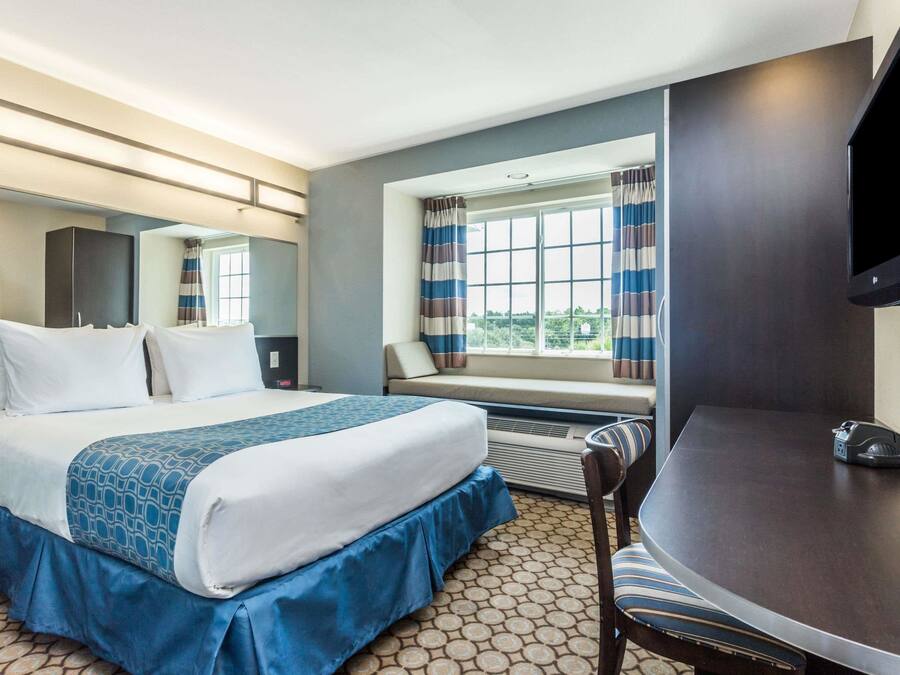 Una habitación de hotel con cama, escritorio, silla, televisor y ventana con cortinas.