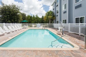 A rectangular swimming pool with a white fence and lounge chairs.