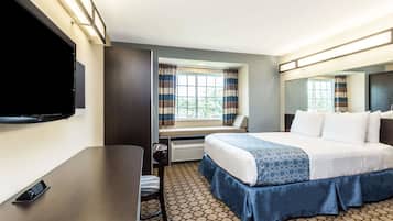 Habitación de hotel con cama, escritorio, silla, televisor y ventana con cortinas.