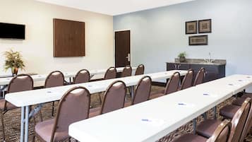 Ein Konferenzraum mit langen Tischen, Stühlen, einem Fernseher, einer Holzeinrichtung und gerahmten Bildern an der Wand.