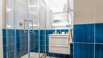 Un baño con cabina de ducha de vidrio, azulejos azules y blancos, un lavamanos blanco y un espejo encima.