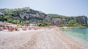 A pebble beach with umbrellas and sun loungers, a clear view of the sea, and buildings on a cliff. - Le Ancore (Vico Equense)