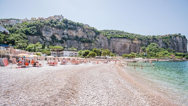 A pebble beach with umbrellas and sun loungers, a clear view of the sea, and buildings on a cliff. - Le Ancore (Vico Equense)