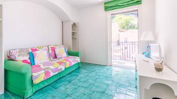Une pièce avec un canapé vert, un bureau blanc et un balcon offrant une vue dégagée.