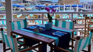 An outdoor seating area with striped chairs and tables, overlooking a marina with boats and umbrellas. - Le Ancore (Vico Equense)