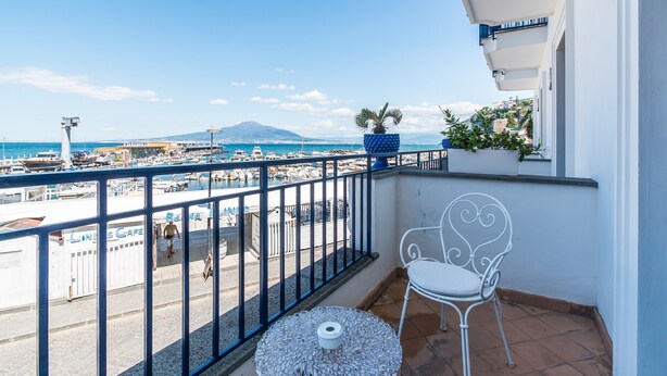 A balcony with a view of the sea, a white chair, a small table, and potted plants. - Le Ancore (Vico Equense)