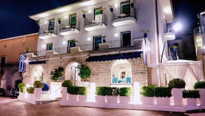 A hotel with a stone facade, multiple balconies with plants, and a well-lit entrance. - Le Ancore (Vico Equense)