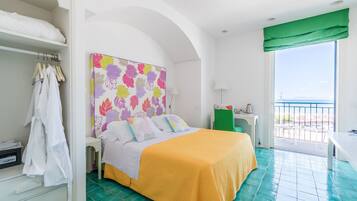Habitación de hotel con cama, una silla verde, escritorio y balcón con vistas.